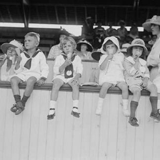 Children sit on wall in front of stands at the ballpark and eat ice cream cones