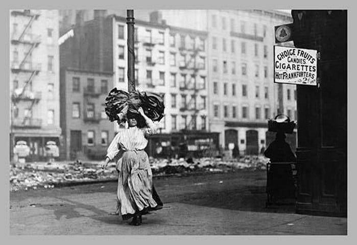 Immigrant Woman Walks Down Street Carrying a Pile of Clothing on Her Head