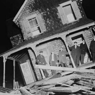 Men stand on Porch of a Sea bright Cottage torn from its foundation and tilted at a 45 degree angle