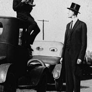 Photographer Mounts himself on the roof of a car to shoot a pictures of an exceedingly tall men in a top hat
