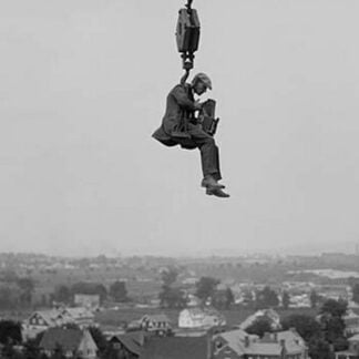 Still Photographer hangs suspended high above the ground on the hook of a large crane