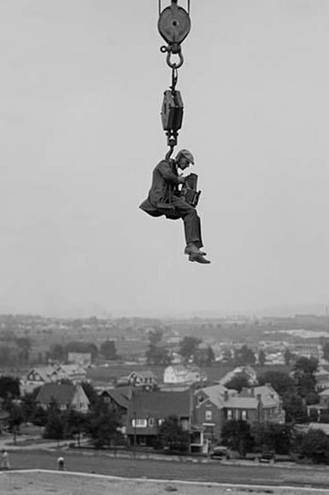 Still Photographer hangs suspended high above the ground on the hook of a large crane